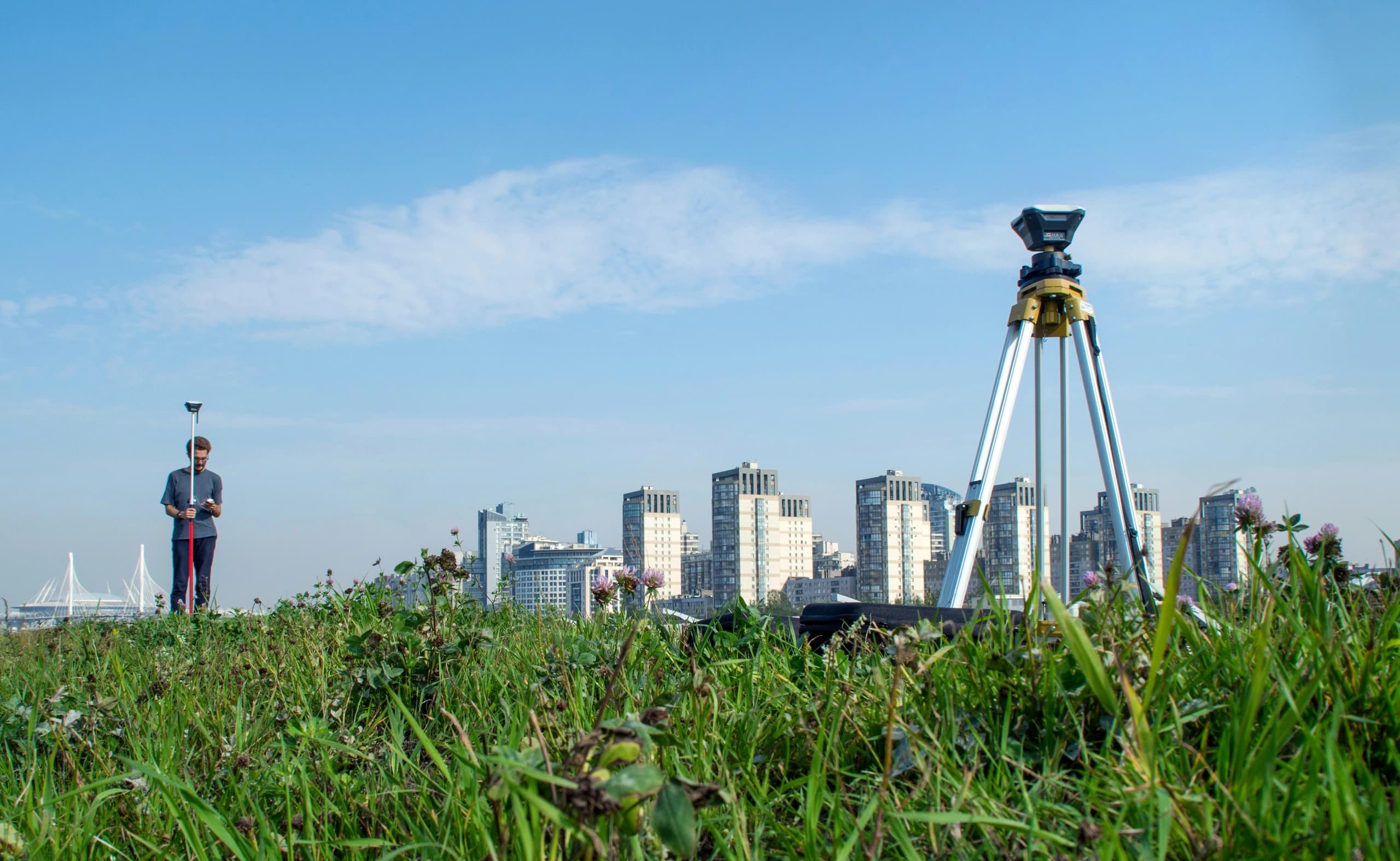 Survey instrument on a tripod in long grass, a city skyline on the horizon behind