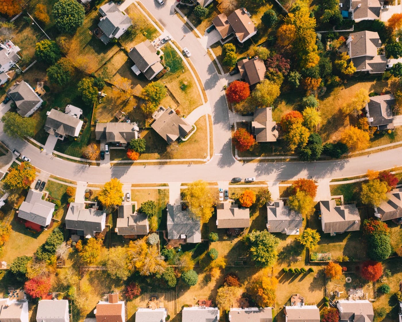 Aerial view of a suburban neighborhood in autumn, showing curving streets, pitched roofs and mature trees