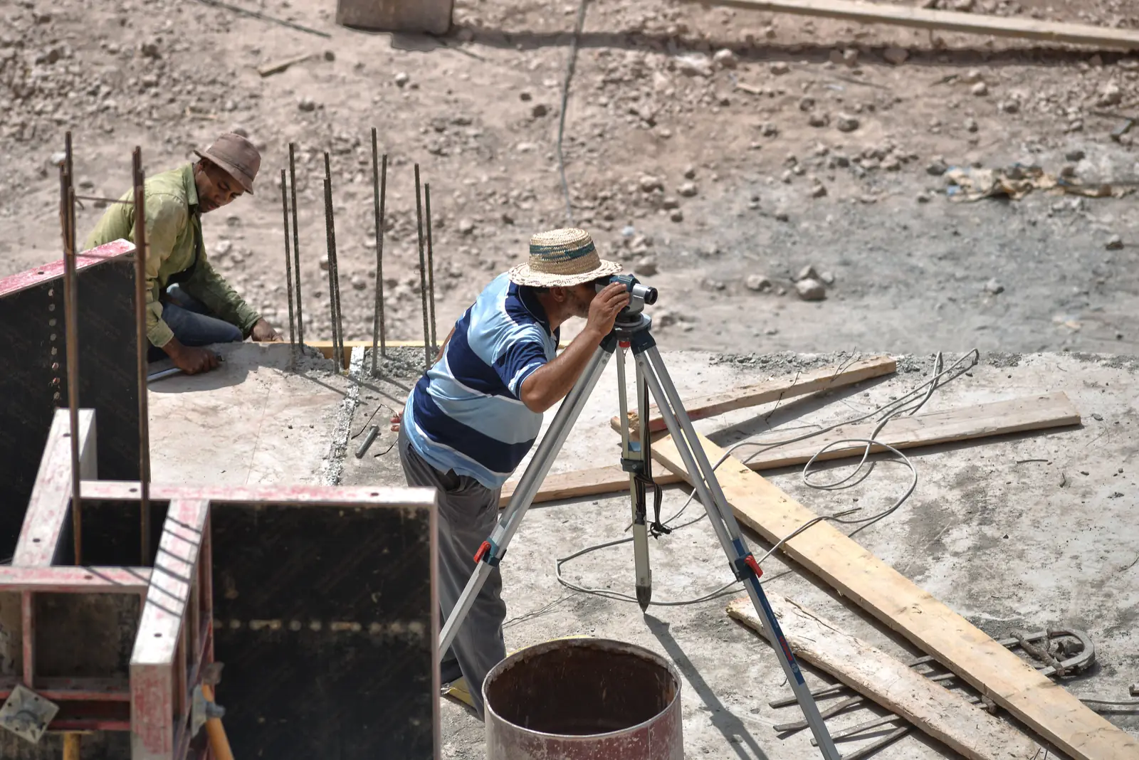 Surveyor sighting through a levelling instrument on a tripod beside rebar and formwork on a concrete pour